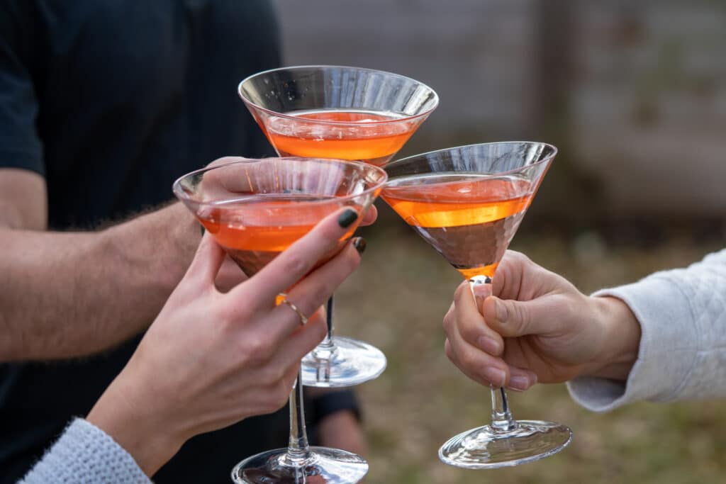 Close-up of three arms holding cocktails in martini glasses together in a toast.